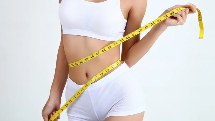 Frau misst Taille mit Maßband Frau legt gelbes Maßband um Taille.