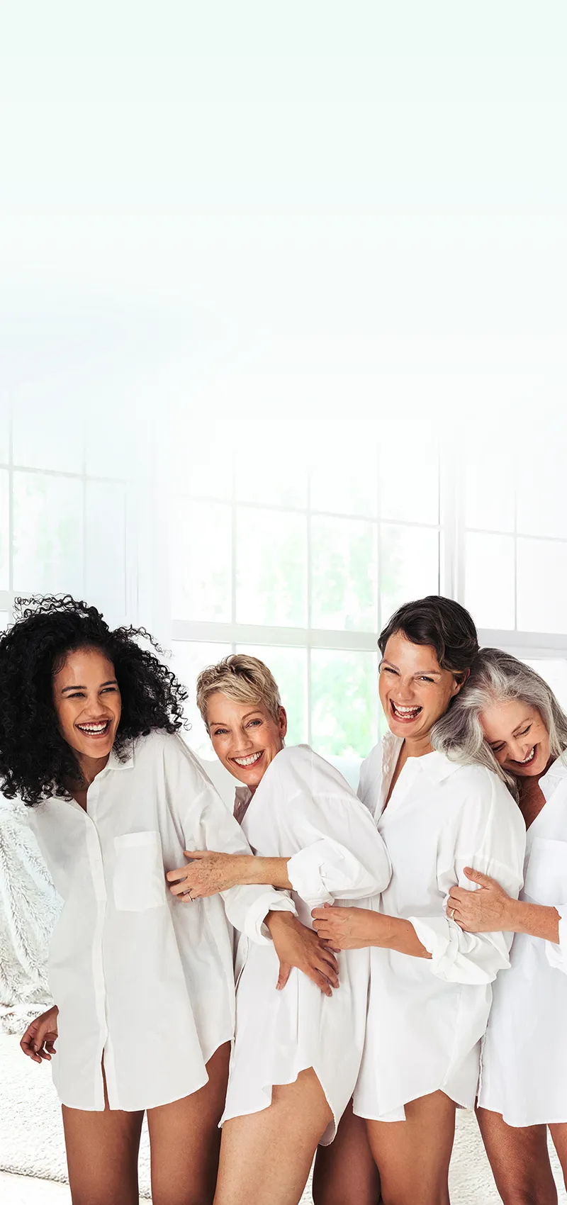 Gruppe lachender Frauen in weißer Kleidung Vier Frauen in weißer Kleidung lachen zusammen in heller Umgebung.